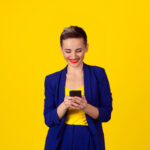 Happy young woman holding using new smartphone connected browsing internet worldwide isolated on yellow wall background. 4g data plan provider Happy young woman holding using new smartphone connected browsing internet worldwide isolated on yellow wall background. 4g data plan provider